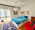 bedroom with bed, rug, two chairs, nightstand, three paintings, lamps, curtains