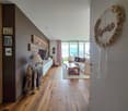 Living room with wooden floor, white walls, large windows, couch, coffee table, lamp, TV, wooden decorations, framed pictures, and a rug.