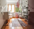 Spacious kitchen with hardwood floors, white cabinets, stainless steel appliances including a dishwasher, and a decorative kitchen rug on the floor.