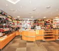 Cosmetic store with numerous shelves and cabinets full of products, a wooden reception counter with a glass top, modern lighting fixtures on the ceiling, and a checkered floor.