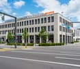 Modern office building with a Migros sign on top, multiple windows, and a glass entrance.