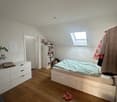 bedroom with bed, white furniture, wooden floor, skylight, storage boxes, books, plant