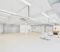Large open warehouse, white walls, concrete floor, industrial shelving on the right, various trolleys and storage boxes scattered