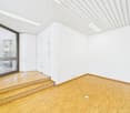 Empty room with white walls, wooden floor, and a glass door leading to an outdoor area. The ceiling has a white paneled design.