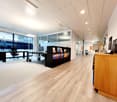 Spacious open-plan office with hardwood flooring, glass partitions, desks, computers, and storage units. The office has a modern and professional design with good natural lighting from the large windows.