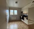 An empty kitchen with white tiles, white cabinets, ceiling light, windows, stove, sink, and countertop.