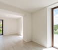 Empty room, white tiles, large glass windows, glass door, balcony with railings, mountain view.
