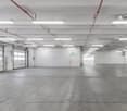 An empty underground parking space, concrete floor, white walls, double garage doors, white pillars, industrial lighting, utility boxes