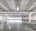 Empty parking lot with concrete floor, white walls, white ceiling, and mounted ceiling lights.