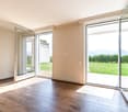Spacious living room with large windows overlooking a grassy outdoor area, hardwood flooring, and neutral-colored walls.