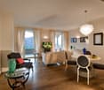 wooden floor, windows, sofa, armchair, dining table with chairs, side table, TV, paintings on wall