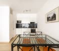 Modern kitchen with white cabinets, black counters, stainless steel appliances, including a microwave, oven, and sink. A picture frame mounted on the wall, glass dining table with chairs.