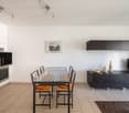 modern dining room with glass table, chairs, white cabinets, tiled floor, black kitchen area, oven, counter, picture frame, TV