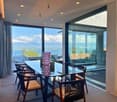 dining table, wooden chairs, glass windows, glass walls, wooden floor, wooden ceiling, mountains, sea, sky