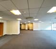 Empty room, white walls, grey carpet, large windows, recessed ceiling lights, doors on both sides