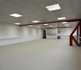 Empty room, white walls, suspended ceiling, red support beams, square ceiling lights
