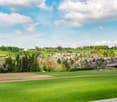 green hills, cluster of houses in the background, trees, blue sky, clouds