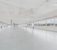 An empty corridor with large windows, white walls and ceilings, and tiled flooring