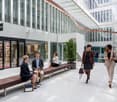 Modern office building with glass walls, people sitting on benches, and people walking through the courtyard area.
