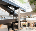 modern building, glass walls, escalators, multiple levels, shops, people walking