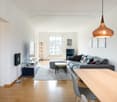 modern living room, gray couch, wooden floor, white walls, TV, entertainment center, dining table, chairs, pendant light