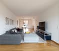 modern living room with gray sofa, wooden floor, white walls, TV, entertainment center, rug, and decorative items
