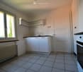 Clean and empty kitchen with white tiles, black and white stove, sink, wooden window and radiator.