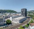 industrial building with solar panels, modern office building, older architectural style buildings, train tracks, parked cars, greenery