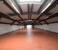 large empty room, red floor, metal roof, metal wall structures, skylights, large doors