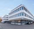 modern office building, white exterior, large windows, multiple floors, parking lot in front