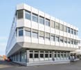 3 story white office building, many windows, parking place