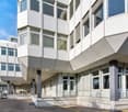 modern office building, white exterior, large windows, multiple floors, concrete base, entrance with stairs