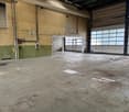 Empty warehouse with concrete floor, green and beige walls, large white doors, no equipment visible
