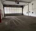 A large open garage with a large glass door, high ceilings, and a concrete floor