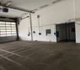 large empty room with concrete floor, two garage doors, two small entry doors