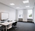 Empty room with white walls, black carpet, long white table, white chairs, white board, two windows with white radiators
