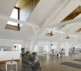gym room with wooden floor, white walls, wooden beams, windows, exercise equipment, yoga mats, plants, reception desk, chairs, table