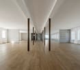 Wide room, wooden floor, white walls, long corridor, white pillars, large arched windows, white radiators