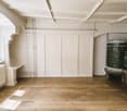 white walls, wooden floors, white radiator, window, two wooden doors