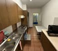 empty kitchen with wooden cabinets, brown tiled floor, stainless steel sink, gas stove, open dishwasher, wooden table, refrigerator
