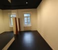 Empty room with black floor, white walls, two windows, radiators, and a mirror.