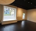 Empty room with large window, radiator, black floor, white walls, window seat, exit sign