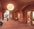 Large indoor space with arched doorways, wooden beams on the ceiling, and a large chandelier. Several people are seated and walking through the hallway.