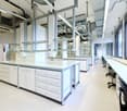 Modern laboratory, white cabinets, large glass shelves, large glass windows, black swivel chairs, white countertops, glass dividers, metal railings, fluorescent lights on ceiling