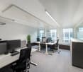 An empty office with desks, computers, chairs, and a plant.