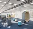 modern office layout with desks, chairs, and small seating pods, white walls, mounted picture frames, carpeted floor
