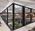 modern office with large glass walls, indoor plants, tiled floor, chairs, tables, people sitting