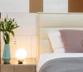 a bedroom with a double bed, nightstand with a lamp and vase, and white walls