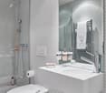white tile wall, white ceramic sink, white toilet, shower head, towel rack, basket with towels