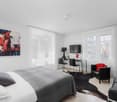 Modern and minimalist bedroom with white walls, wooden floor, large windows with white curtains, double bed, modern nightstand, TV, desk, and a chair